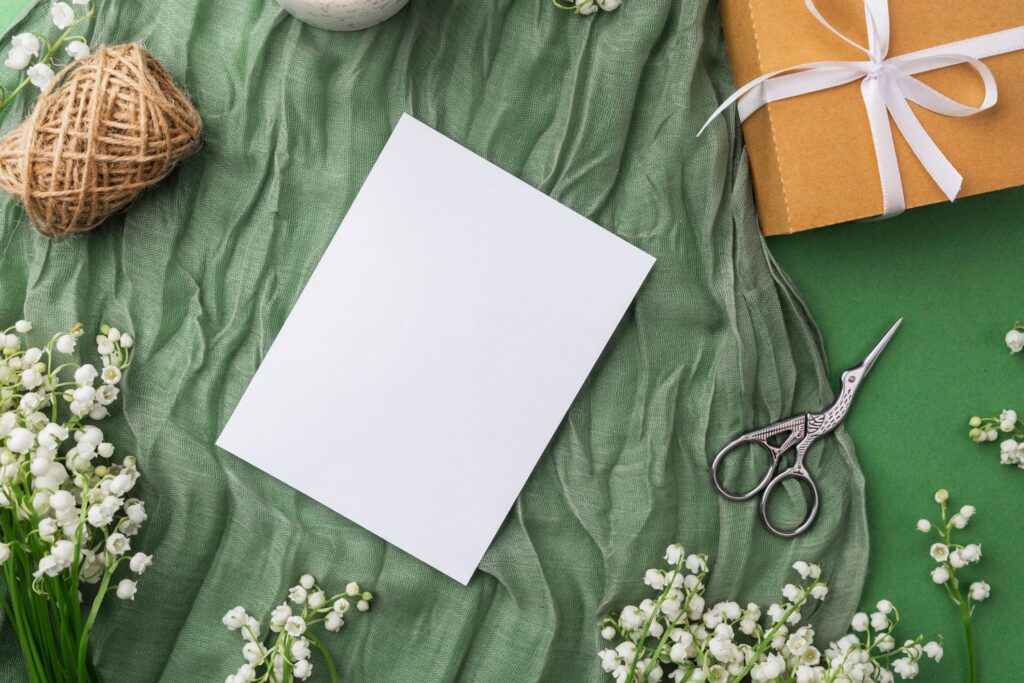 Blank card with candle, gift and spring flowers on green fabric