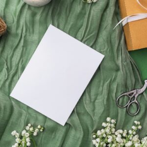 Blank card with candle, gift and spring flowers on green fabric